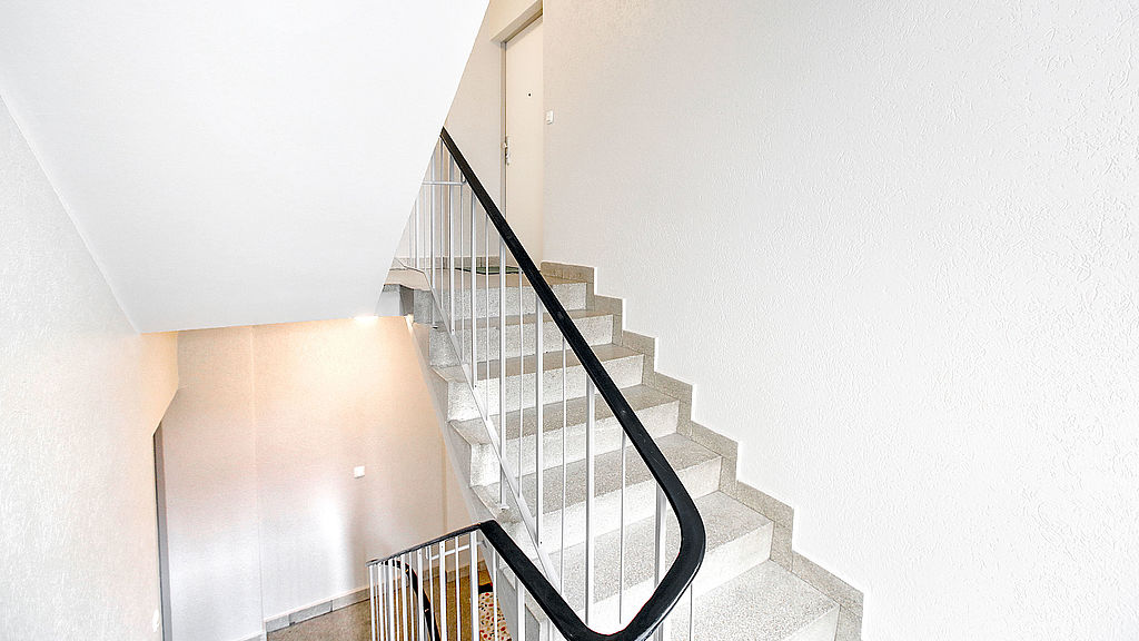Weiß gestrichenes Treppenhaus mit dunklem Handlauf